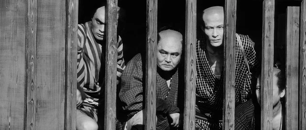 Yojimbo (1961) movie still: medium — Four men peer through vertical wooden slats inside a dimly lit wooden enclosure. They stand close together with…