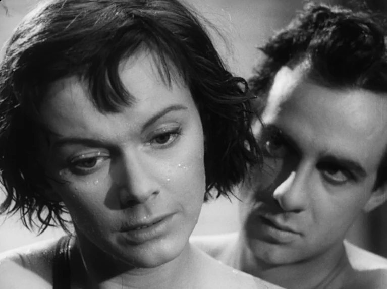 Waiting Women (1952) movie still: closeup — A close up shows a man standing directly behind a woman in a room. Both subjects have intense facial…