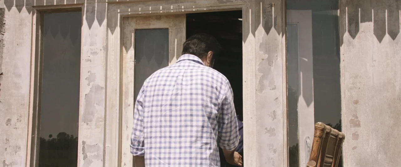 Peranbu (2019) movie still: medium — A weathered white wooden frame surrounds a doorway with peeling paint and architectural trim. A man in a…