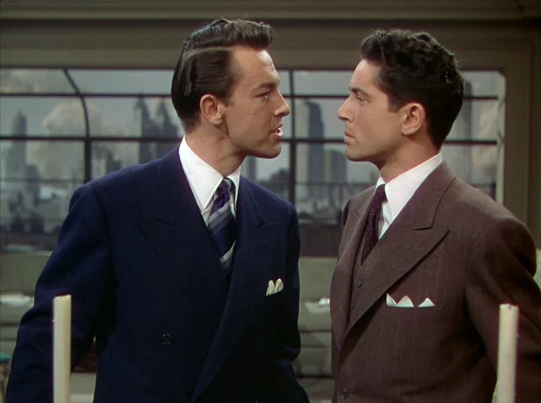 Rope (1948) movie still: medium — A high-rise room with a large window overlooking a gray city skyline. Two men in formal business suits stand close…