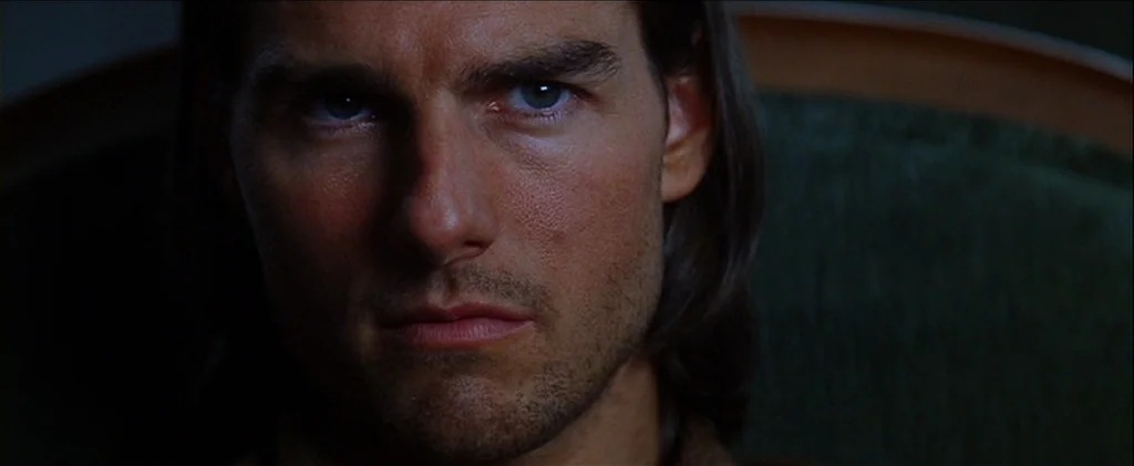 Magnolia (1999) movie still: closeup — A close up view of a man's face in a dimly lit setting. The subject looks directly toward the viewer with a…