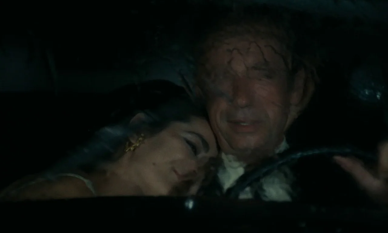 Z (1969) movie still: medium — The interior of a moving car at night is dark and dimly lit. A man drives as a woman rests her head against his…