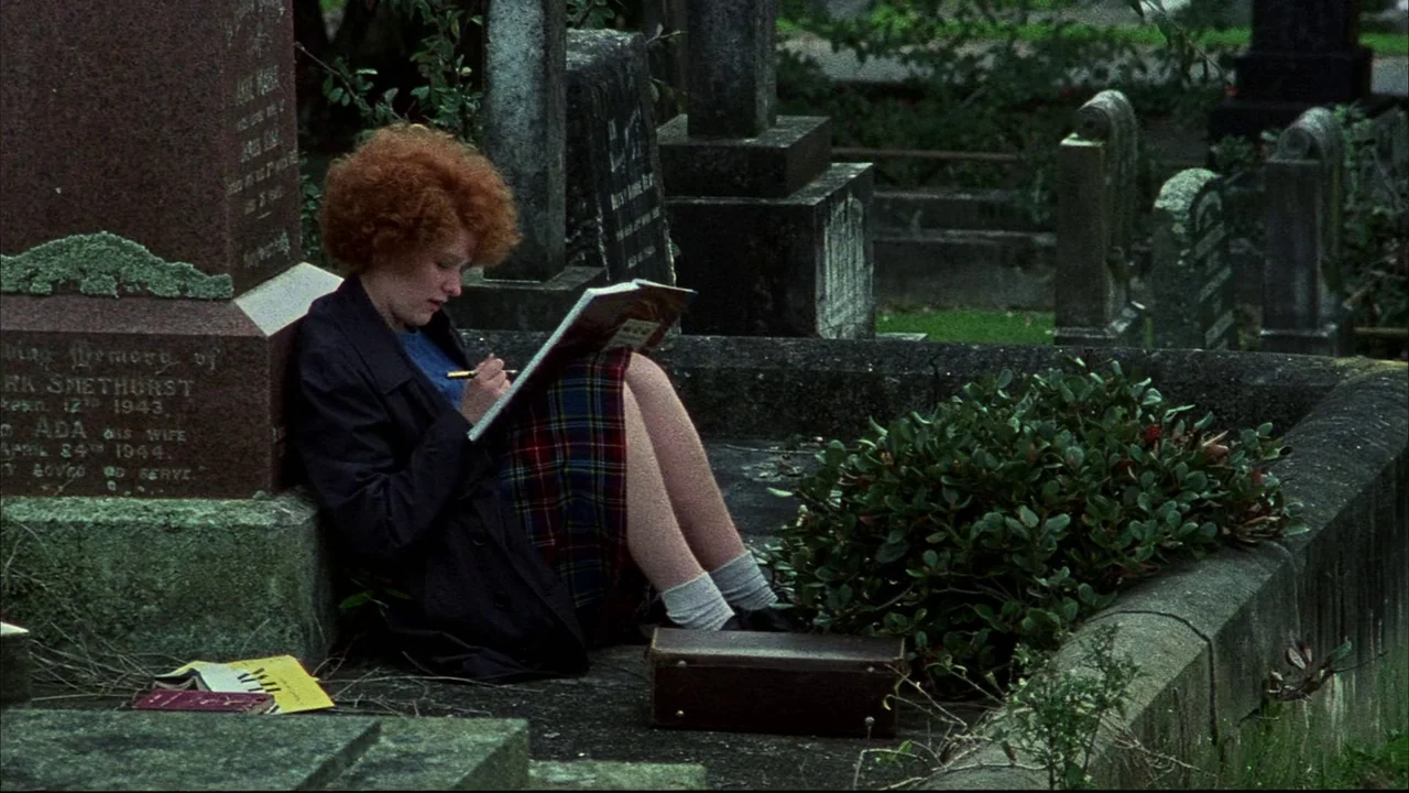 An Angel At My Table (1990) movie still: medium — A quiet cemetery with weathered stone headstones overgrown with moss and dark foliage. A woman…