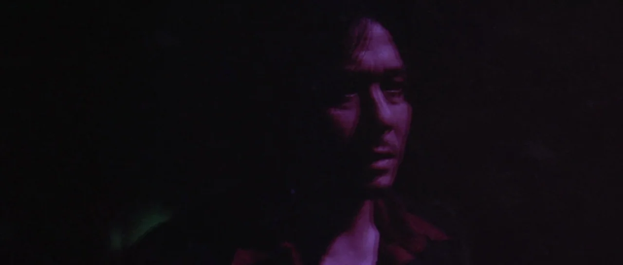 Oldboy (2003) movie still: closeup — A dark, underexposed environment leaves most of the frame in shadow. A man stands partially illuminated by a…