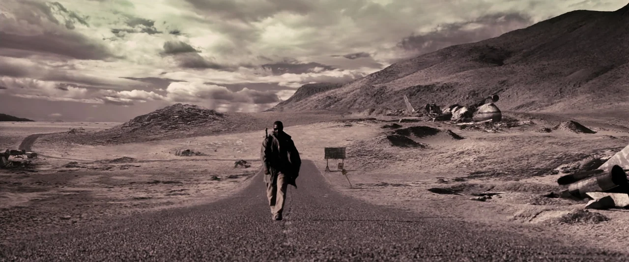 The Book of Eli (2010) movie still: wide — A desolate desert landscape contains a narrow, aging road winding through arid, hilly terrain. A man…