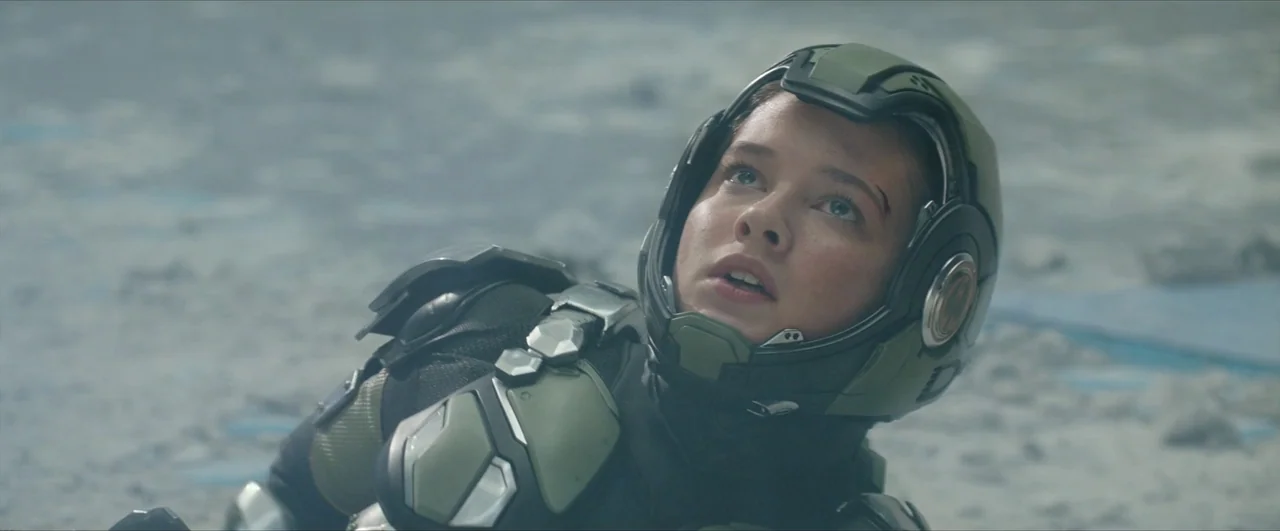 Pacific Rim: Uprising (2018) movie still: closeup — A barren, rocky, light-gray landscape stretches out under a clear, bright sky. A young woman…