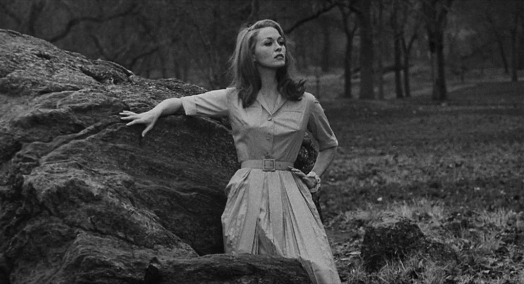 Puzzle of a Downfall Child (1970) movie still: fullbody — A woman stands in a public park with leafless trees and large rock formations. She leans…