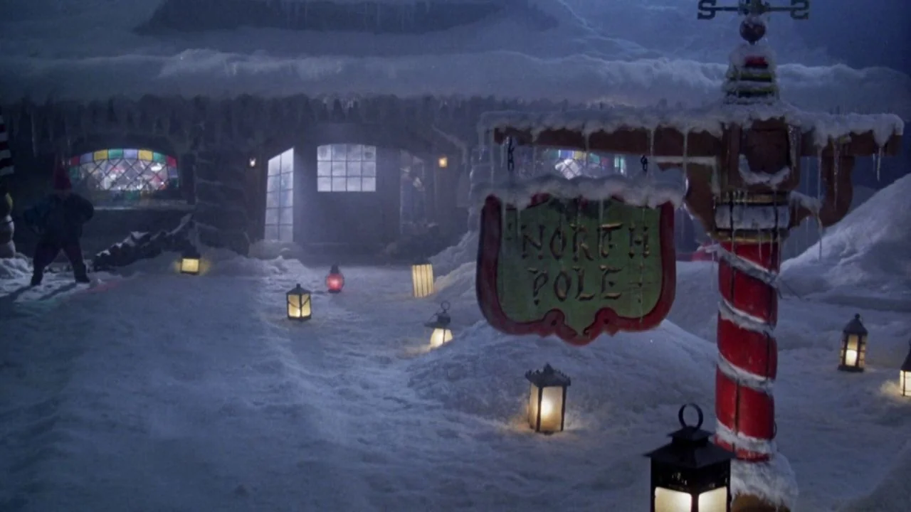 Scrooged (1988) movie still: wide — A snowy outdoor area features a wooden signpost reading North Pole and multiple lanterns. A frosted, lit window…