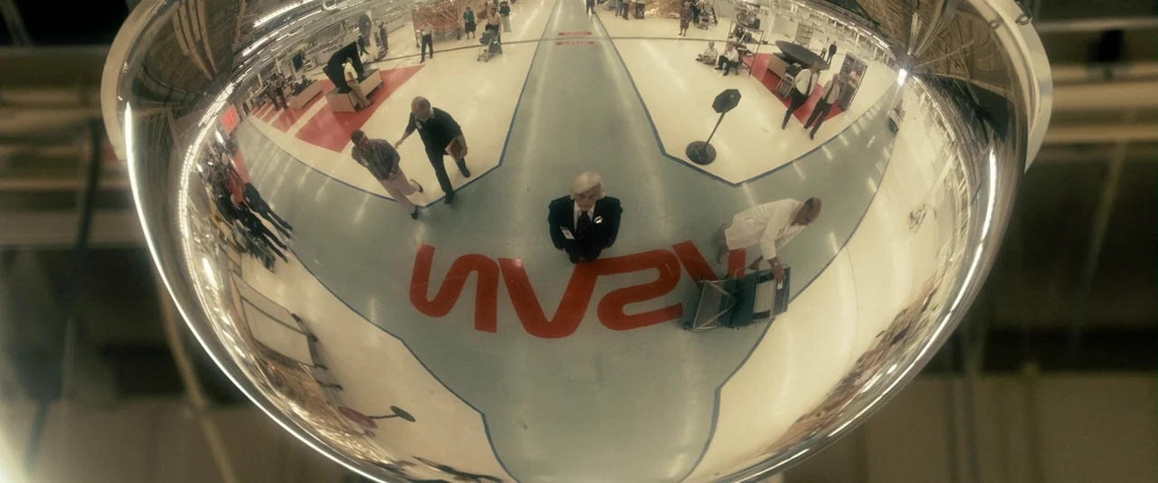The Box (2009) movie still: wide — A wide-angle perspective within a large NASA industrial facility captured by a convex mirror. Multiple employees…