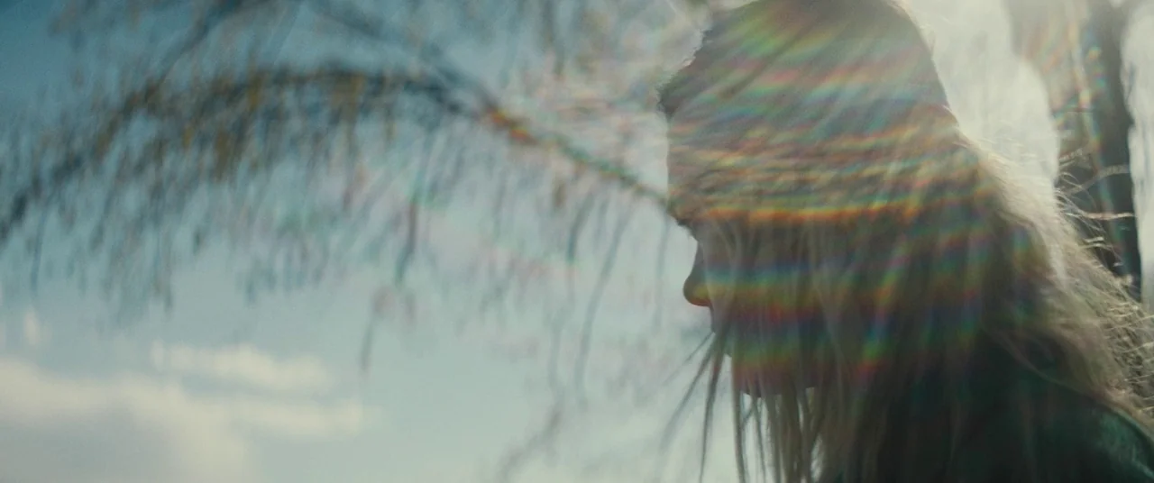 I Think We’re Alone Now (2018) movie still: closeup — A bright outdoor setting with a blurred foreground branch and expansive sky. A young woman…