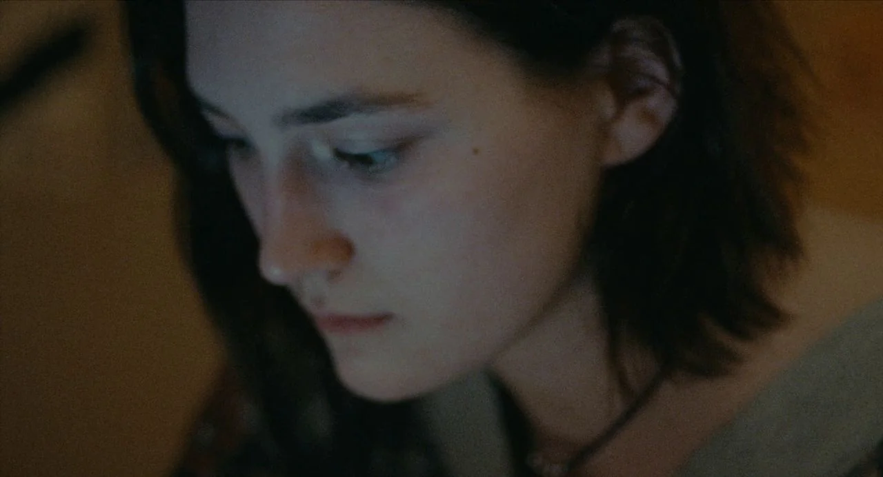 Never Rarely Sometimes Always (2020) movie still: closeup — The face of a young woman is illuminated in a dark, interior space. She looks downward…