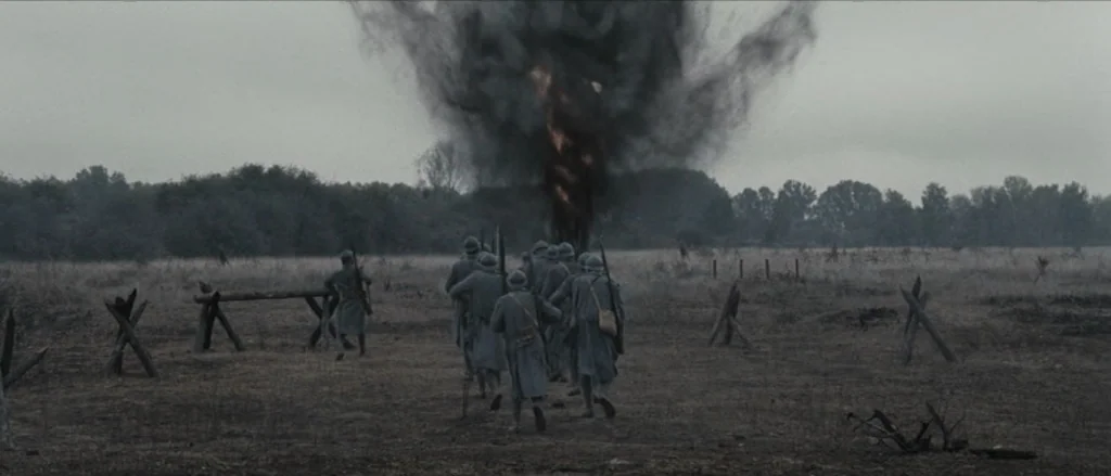 Frantz (2016) movie still: wide — A desolate, war-torn field features wooden anti-tank barriers scattered across dry, sparse vegetation. A group of…