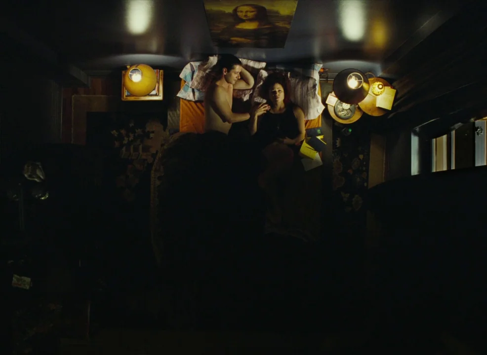 Laurence Anyways (2012) movie still: wide — A dimly lit room viewed from directly above reveals a couple in bed. The Mona Lisa print is centered on…