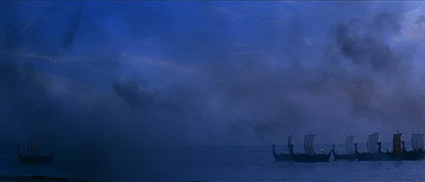 Erik The Conqueror (1961) movie still: establishing — Several wooden viking longships with sails are afloat on dark, calm ocean waters. A heavy,…