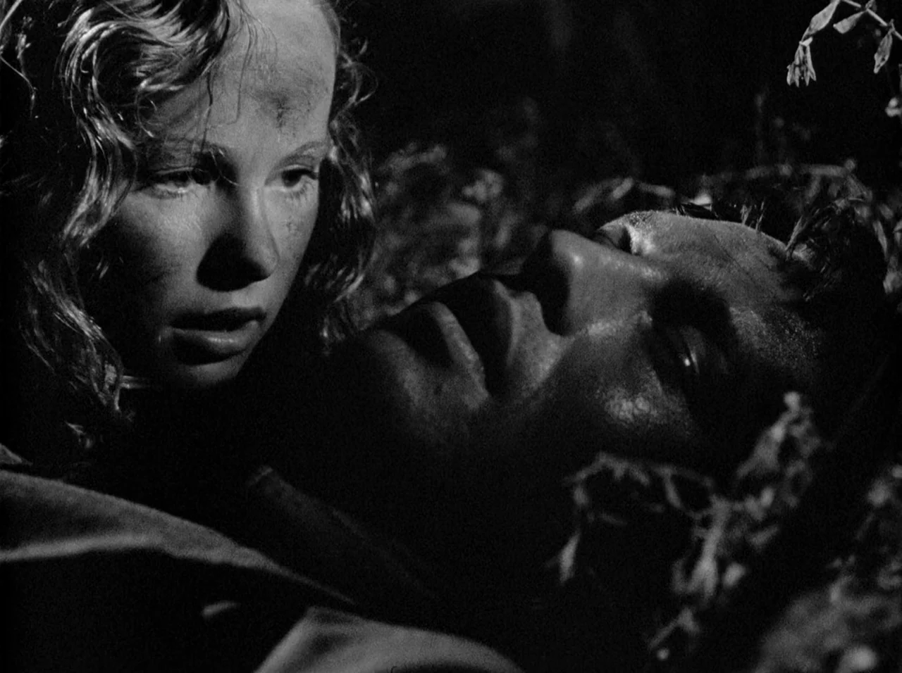 Gun Crazy (1950) movie still: closeup — A woman looks down at a man resting on the ground at night. Low-key lighting highlights the features of…