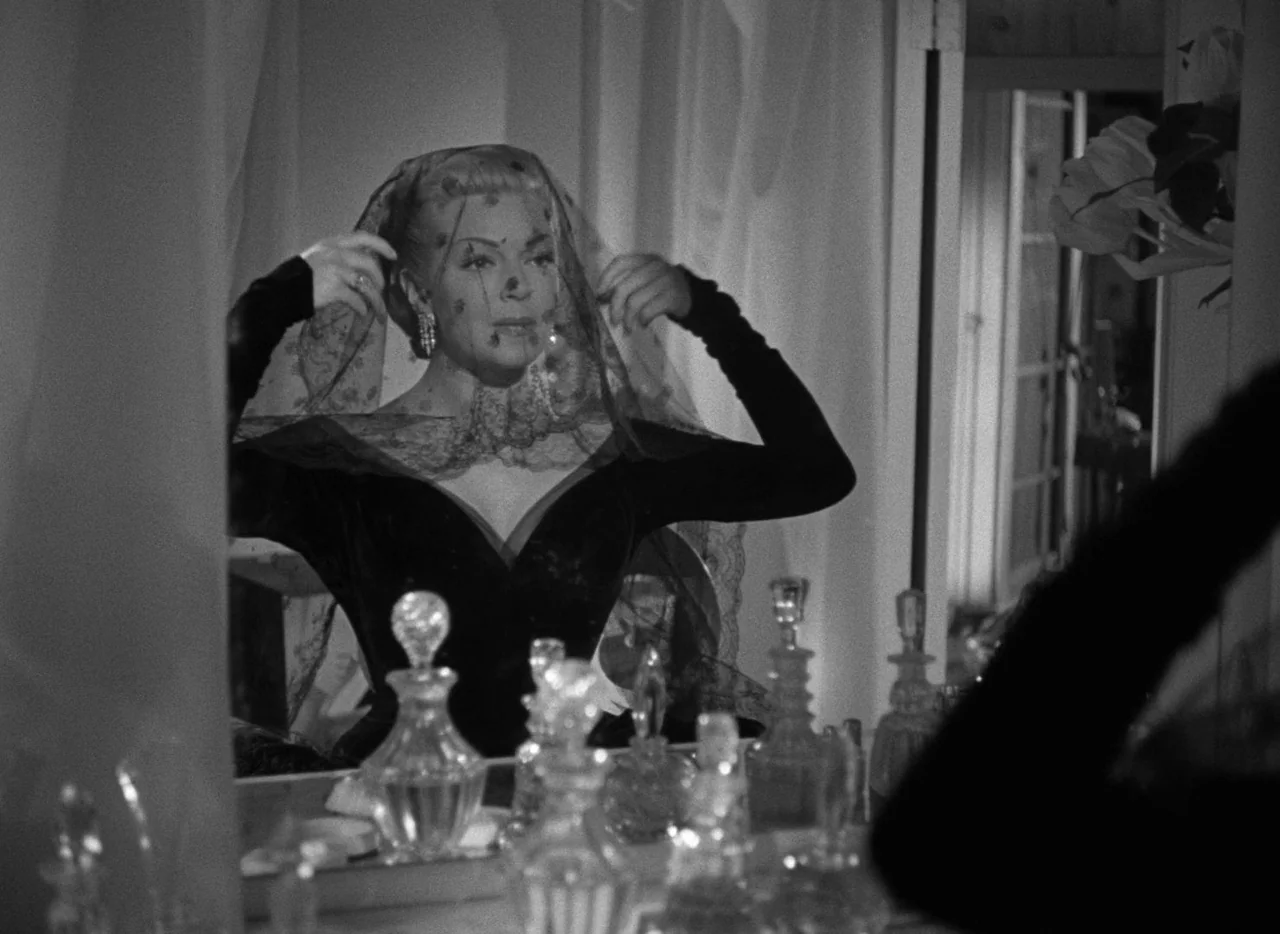 The Bad and the Beautiful (1952) movie still: medium — A woman sits before a mirror on a vanity table surrounded by glass bottles. She adjusts a…