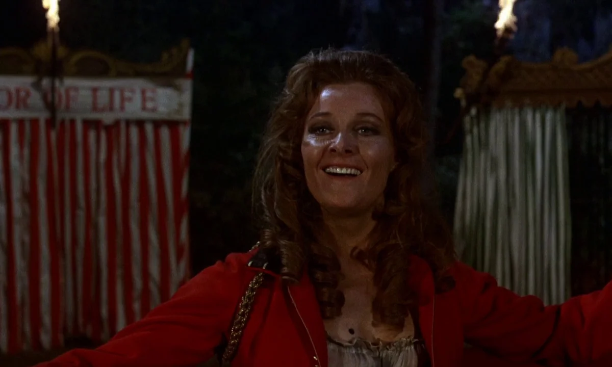 Vampire Circus (1972) movie still: medium — A dark outdoor area features carnival signage reading 'OR OF LIFE' on striped canvas. A woman in a red…