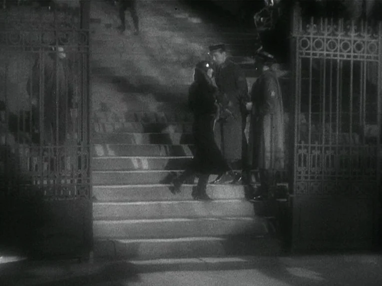 Mata Hari (1931) movie still: wide — Stone stairs lead upward between decorative metal gate structures at night. A woman in a dark coat walks up the…