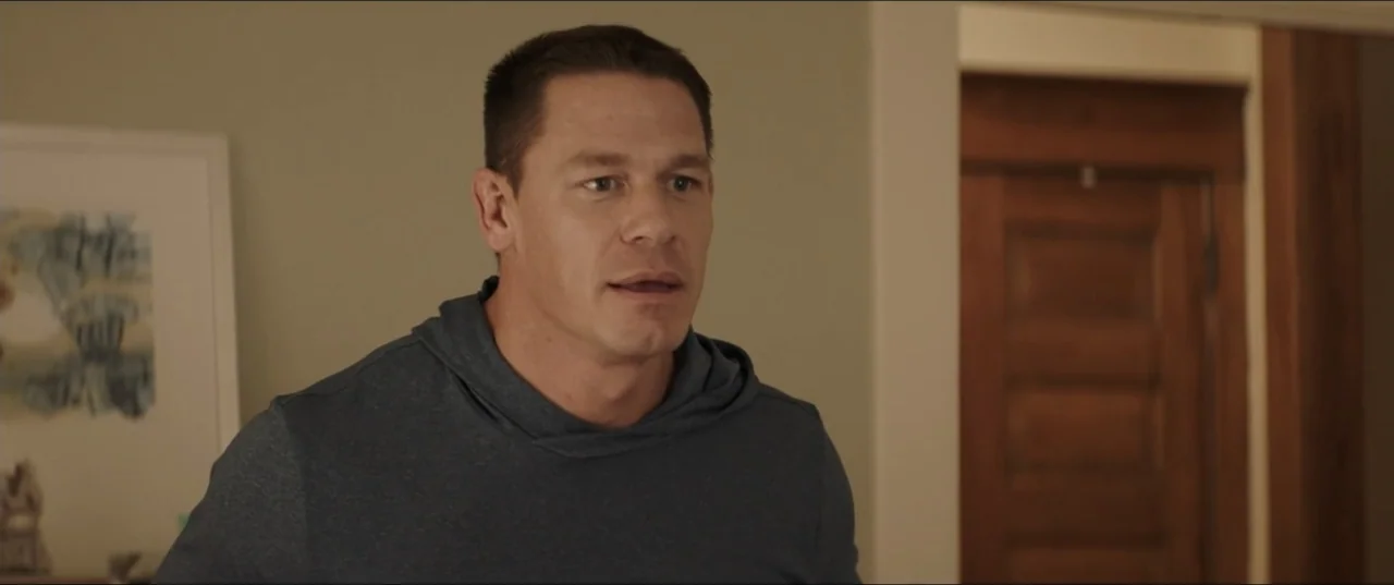 Blockers (2018) movie still: medium — A residential room features neutral-toned walls and a partially visible wooden door. A man in a blue hoodie…