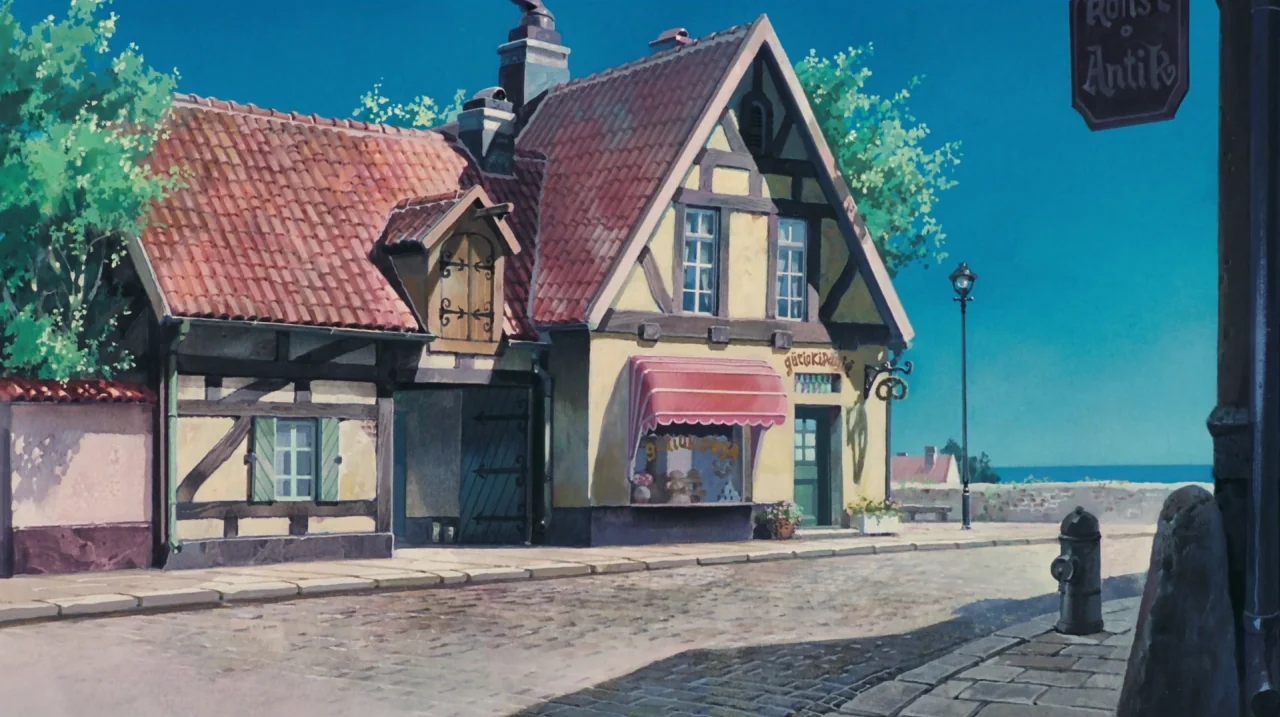 Kiki’s Delivery Service (1989) movie still: establishing — A European-style half-timbered building sits on a quiet cobblestone street under blue…