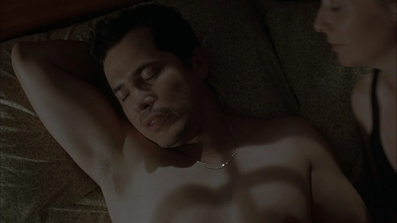 The Babysitters (2008) movie still: medium — A dark bedroom with patterned beige sheets and pillows visible under the characters. A man lies asleep…