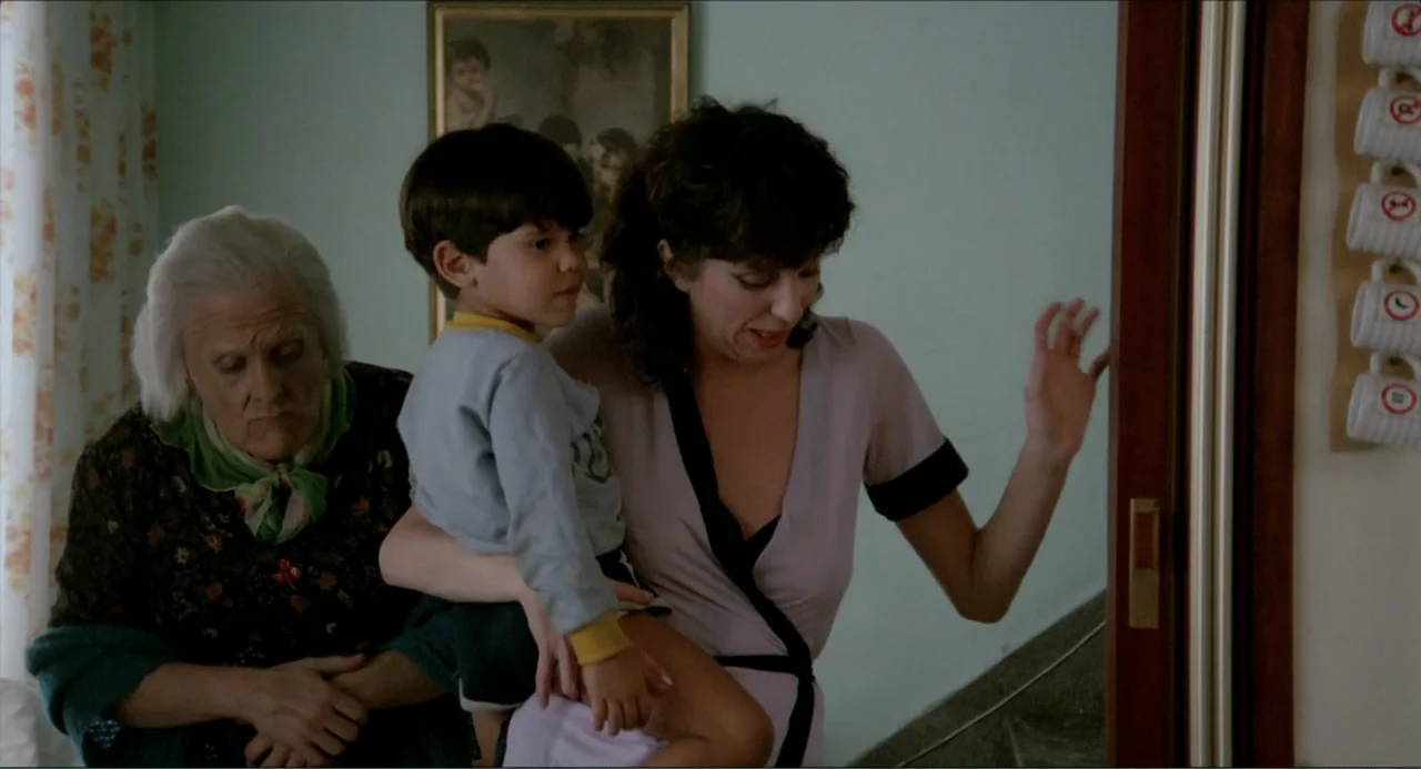 Waiting for the Hearse (1985) movie still: medium — An interior space features light blue walls adorned with a vintage framed print. An adult woman…