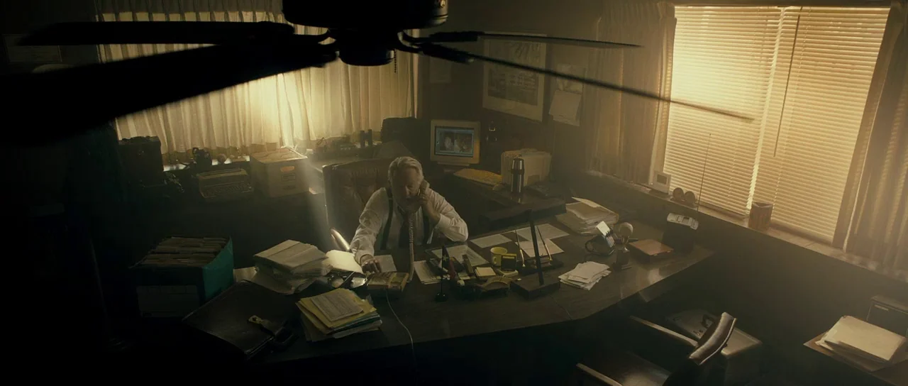 The Imposter (2012) movie still: wide — A cluttered 1990s workspace features a large wooden desk covered in papers and equipment. An older man in a…