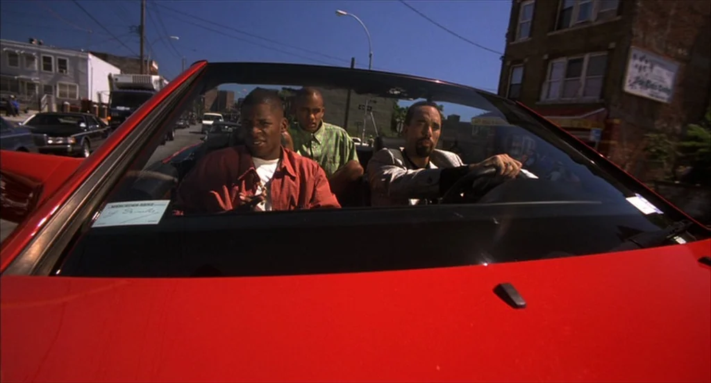 He Got Game (1998) movie still: medium — Three men ride in a bright red convertible along a city street during daytime. The vehicle interior shows…