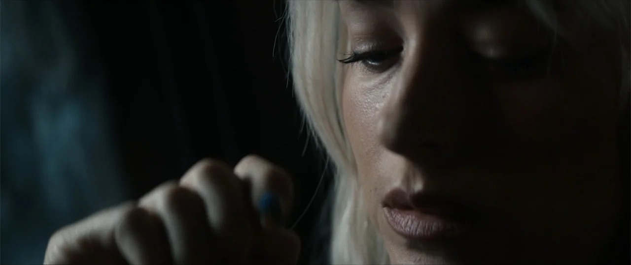 Daddio (2024) movie still: closeup — A close-up view of a woman with white hair in a dimly lit space. She tilts her head downward while holding her…
