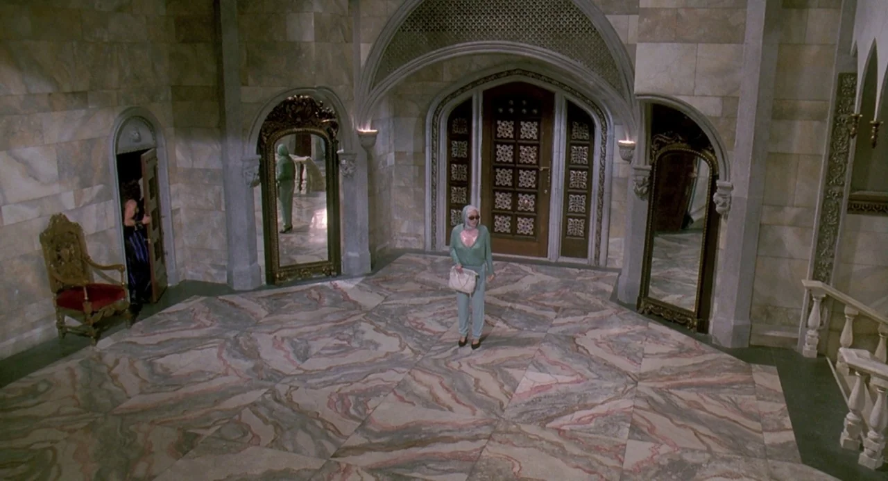 Death Becomes Her (1992) movie still: wide — A spacious marble-floored foyer features decorative mirrors and heavy stone wall arches. A woman stands…
