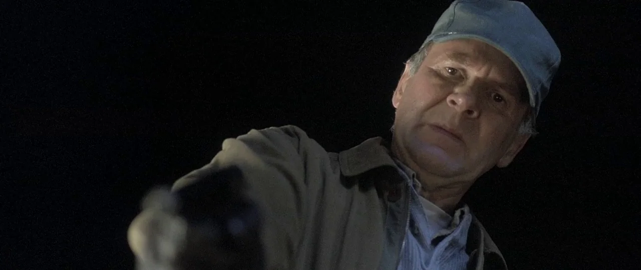 In the Bedroom (2001) movie still: closeup — An older man stands outdoors at night, surrounded by total darkness. He points a small handgun directly…
