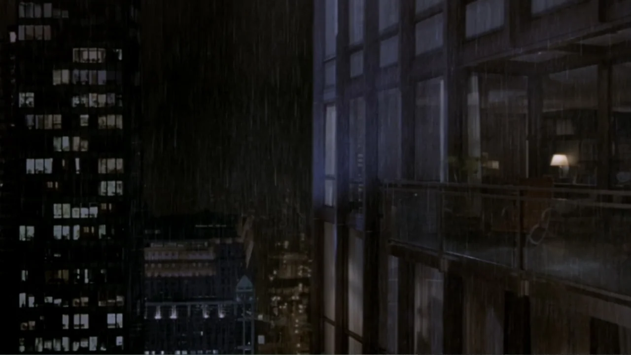 What Women Want (2000) movie still: establishing — A dark urban exterior shows skyscrapers at night under heavy rain during a storm. Glass balconies…
