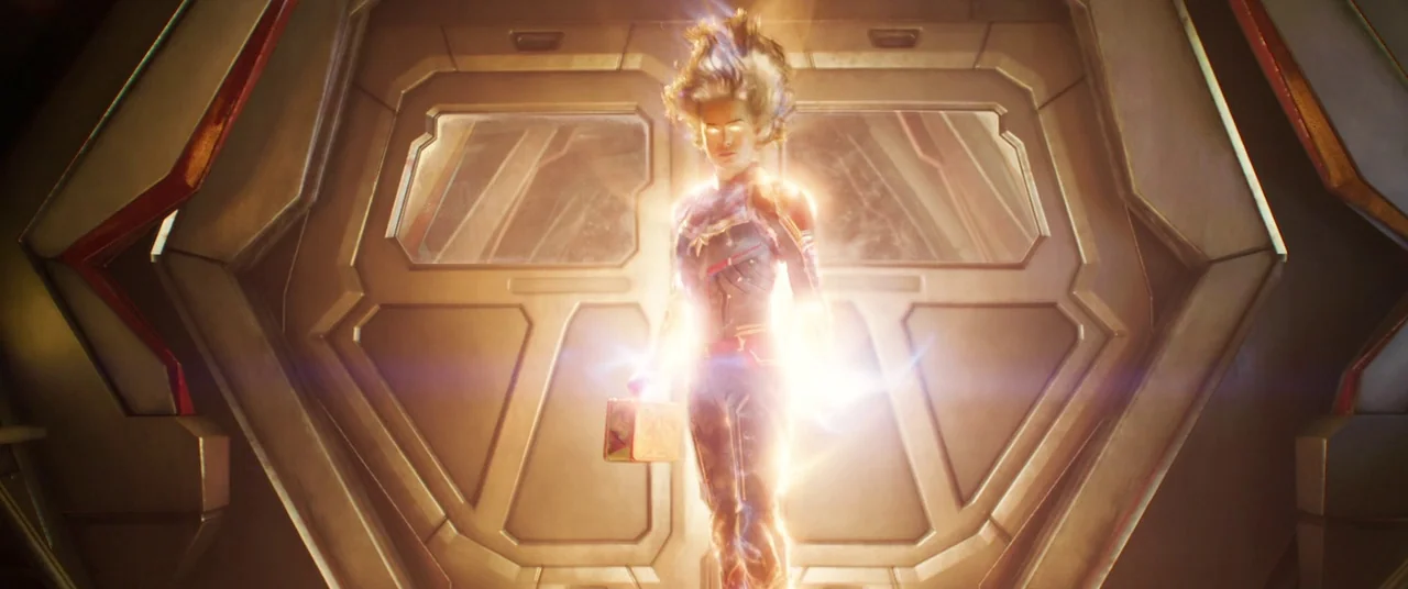 Captain Marvel (2019) movie still: fullbody — A metallic interior corridor with geometric door frames and panels lining the walls. A woman in a…