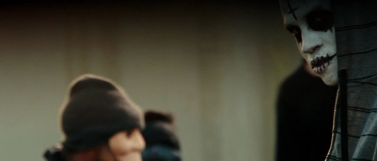 The Purge: Anarchy (2014) movie still: medium — A dimly lit outdoor urban space at night with indistinct blurred background features. A person with…