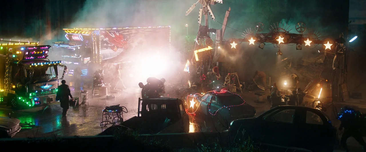 Prisoners of the Ghostland (2021) movie still: wide — A cluttered outdoor junkyard is filled with various old vehicles and scrap metal parts.…