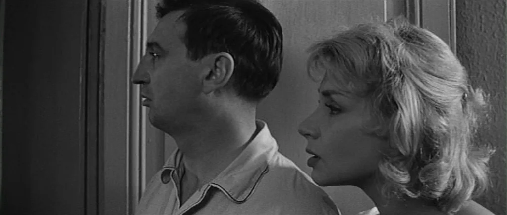 The 400 Blows (1959) movie still: medium — A dark indoor space with a plain wall and a door frame behind them. The man and woman stand side-by-side…