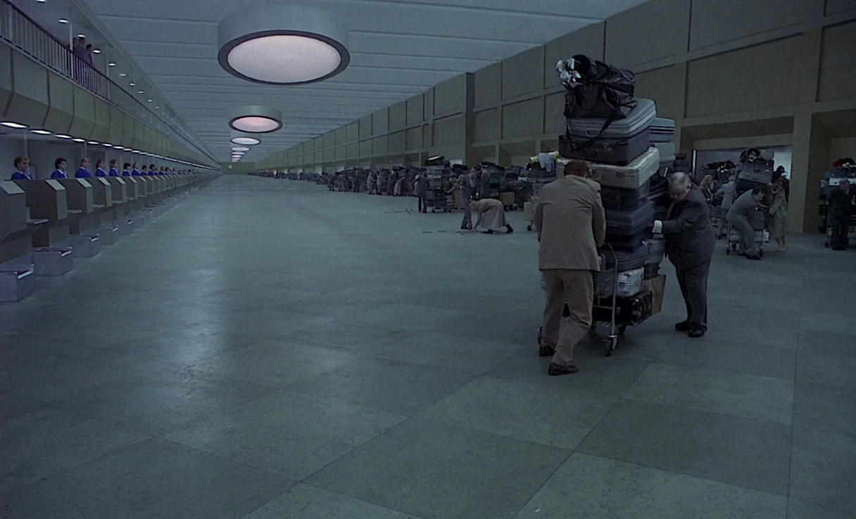 Songs from the Second Floor (2000) movie still: wide — A vast, minimalist airport terminal features a long row of identical service counters. Two…