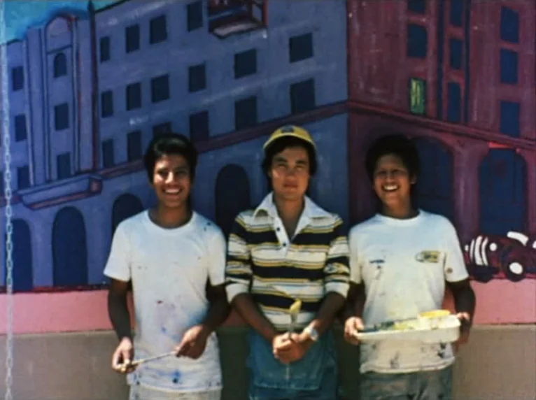 Mur Murs (1981) movie still: fullbody — Three young men stand in a row against a large colorful mural on a wall. They pose together while holding…