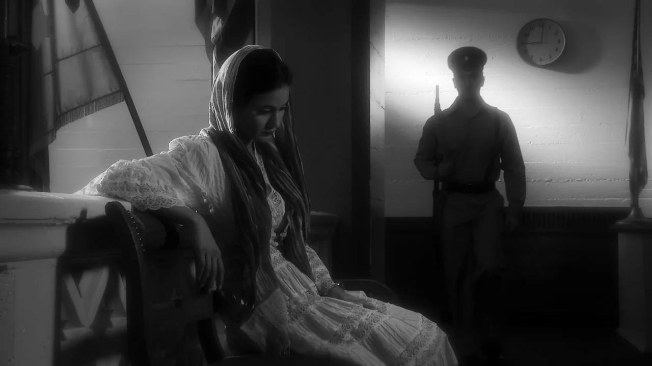 Electra Luxx (2010) movie still: medium — A dimly lit room with flags and a wall clock features wooden furniture. A woman rests on a bench while a…