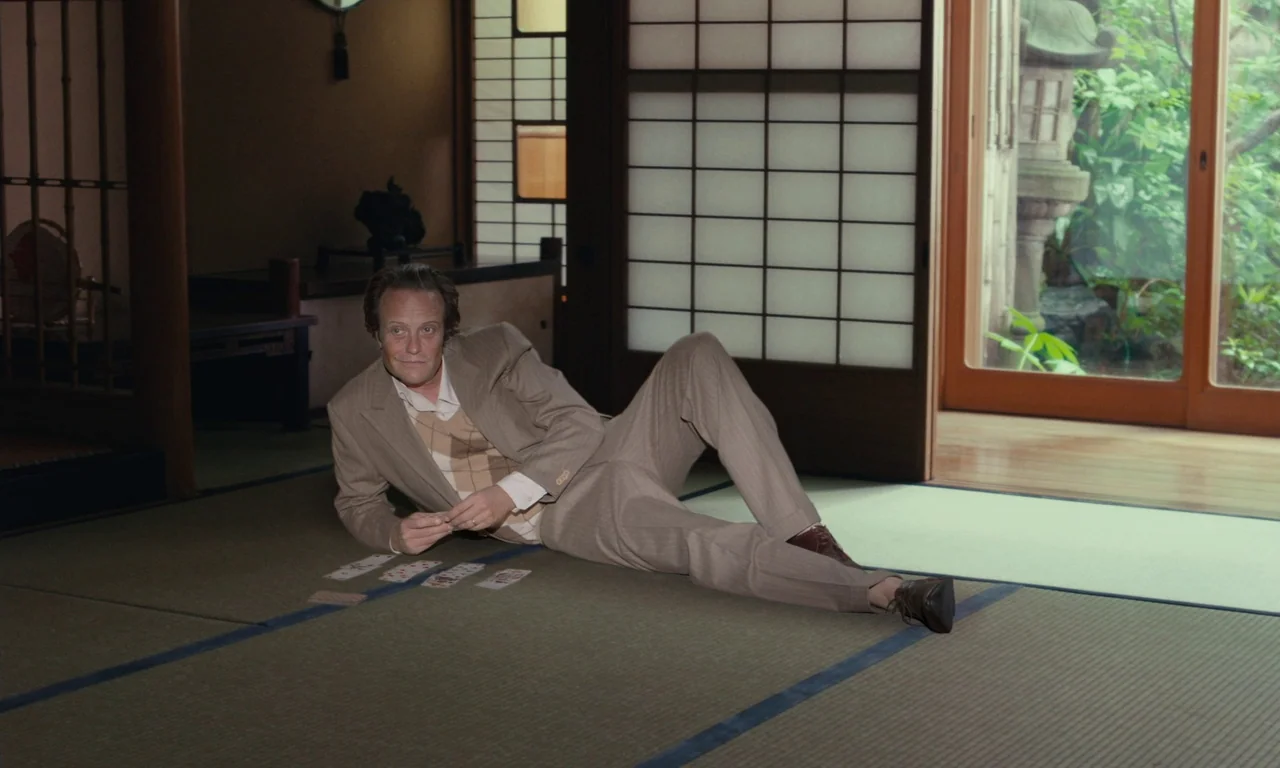 Sidonie in Japan (2023) movie still: fullbody — A Japanese-style room features tatami mats and shoji screens overlooking a small garden. A man in a…