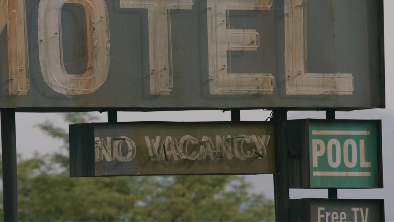 Boy (2010) movie still: medium — A weathered vintage metal motel sign features large letters and neon tubing remnants. The sign displays NO VACANCY…