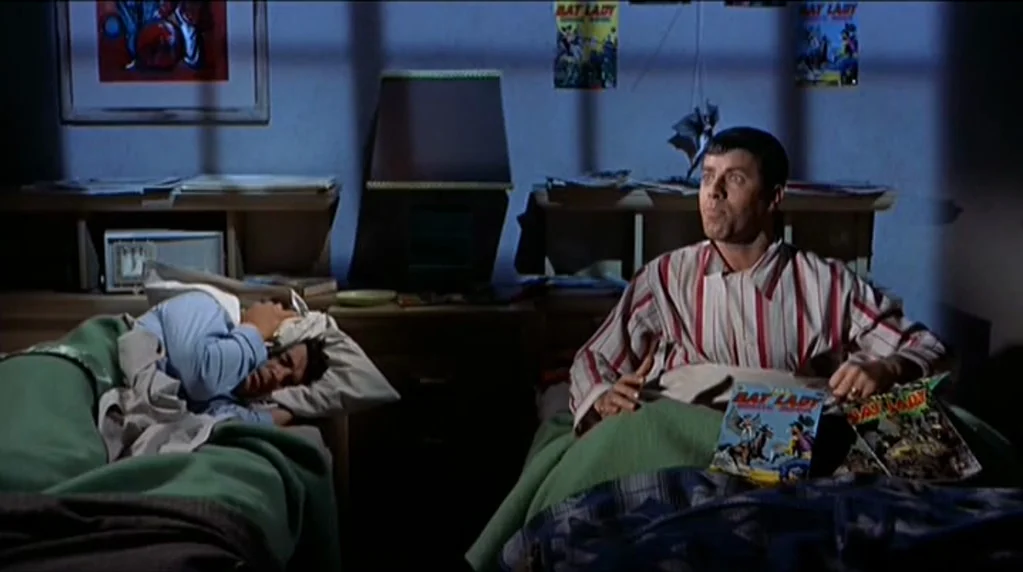 Artists and Models (1955) movie still: medium — A dimly lit room features two beds separated by a bedside table with a lamp. One man sits up holding…