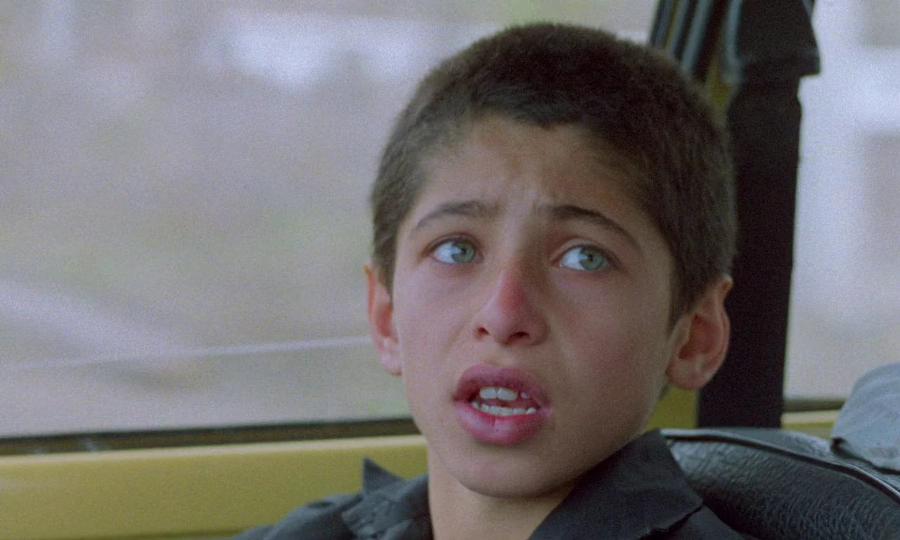 Life, and Nothing More (1992) movie still: closeup — A young boy sits inside a vehicle with yellow interior paneling visible behind him. The boy…