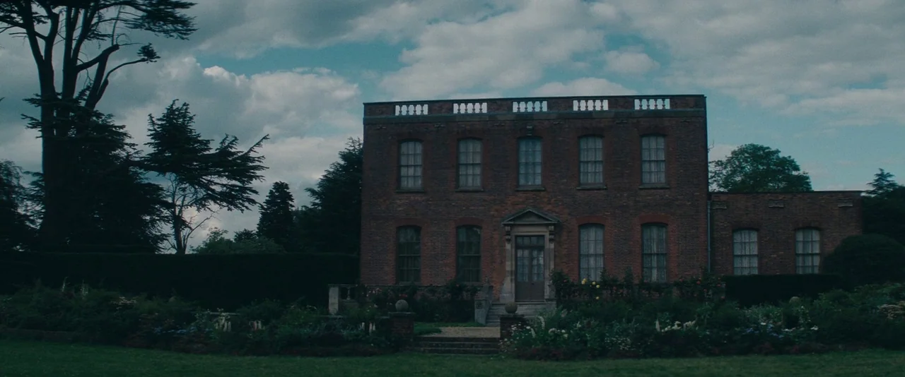 The Invisible Woman (2013) movie still: establishing — A classic brick manor house sits surrounded by a lush lawn and garden. Tall trees frame the…