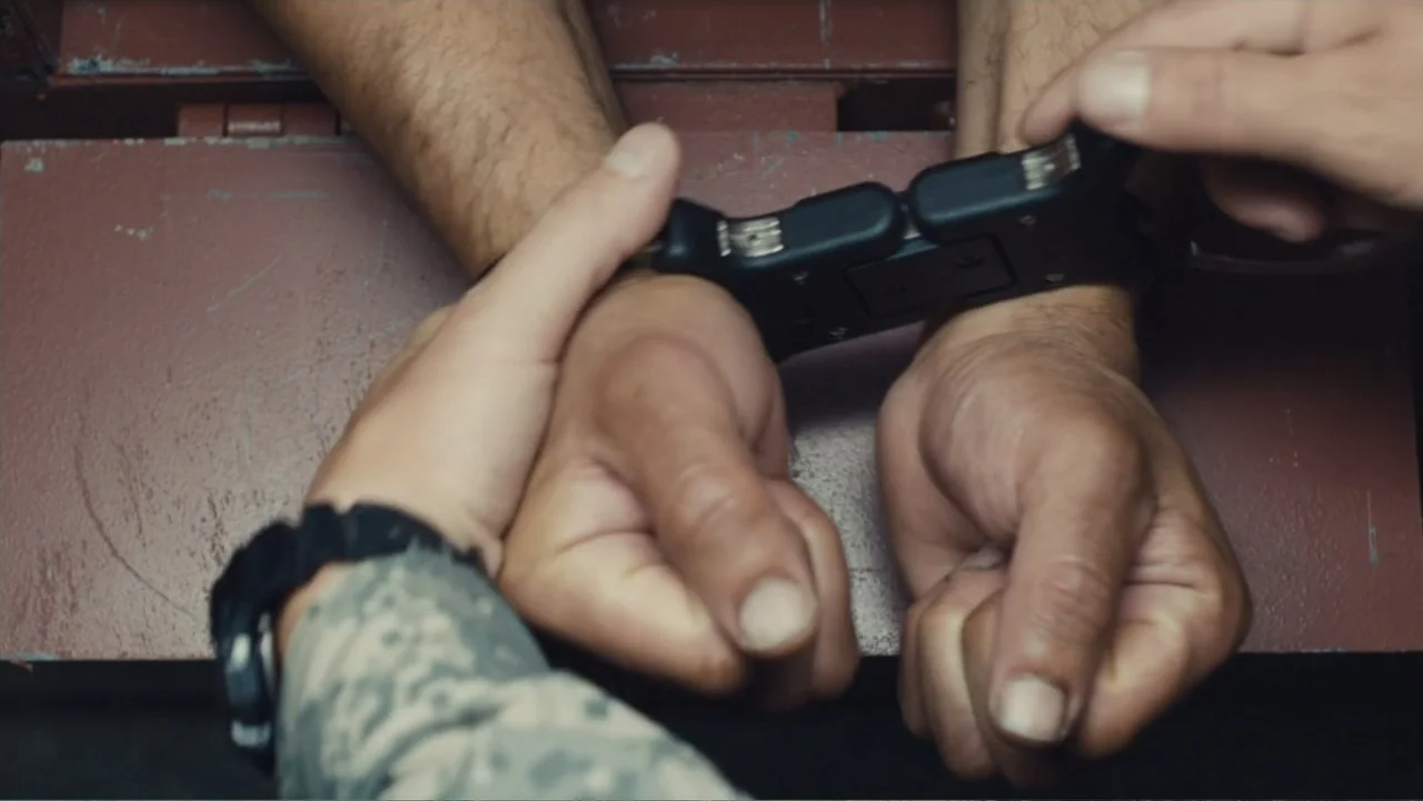 Camp X-Ray (2014) movie still: closeup — A metal table surface provides the backdrop for a subject being restrained. A person's hands secure metal…