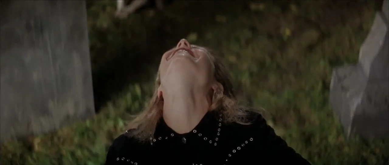 Moonlight and Valentino (1995) movie still: closeup — A night scene set in a grassy cemetery with dark, blurred stone markers. A young woman tilts…
