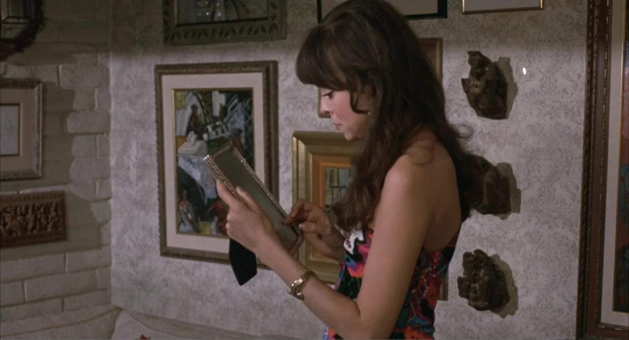 Foxy Brown (1974) movie still: medium — A living room interior featuring light-colored patterned wallpaper and multiple framed pictures on the wall.…