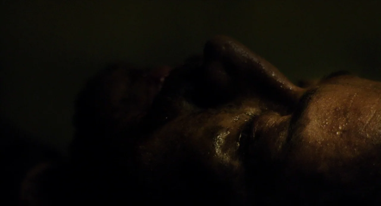 Submergence movie still: closeup — A man's face is partially lit in darkness. He lies in a recumbent position with eyes closed.
