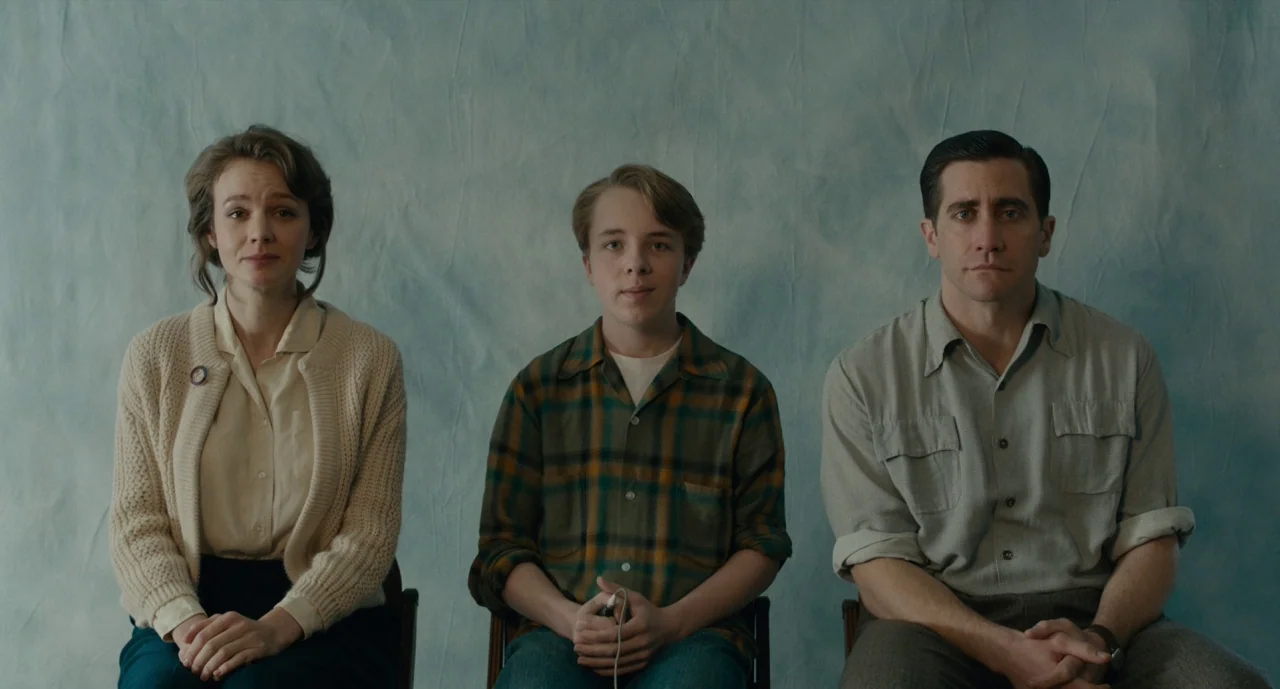 Wildlife (2018) movie still: medium — Three people sit in a row against a textured blue backdrop. They look forward as if posing for a formal…