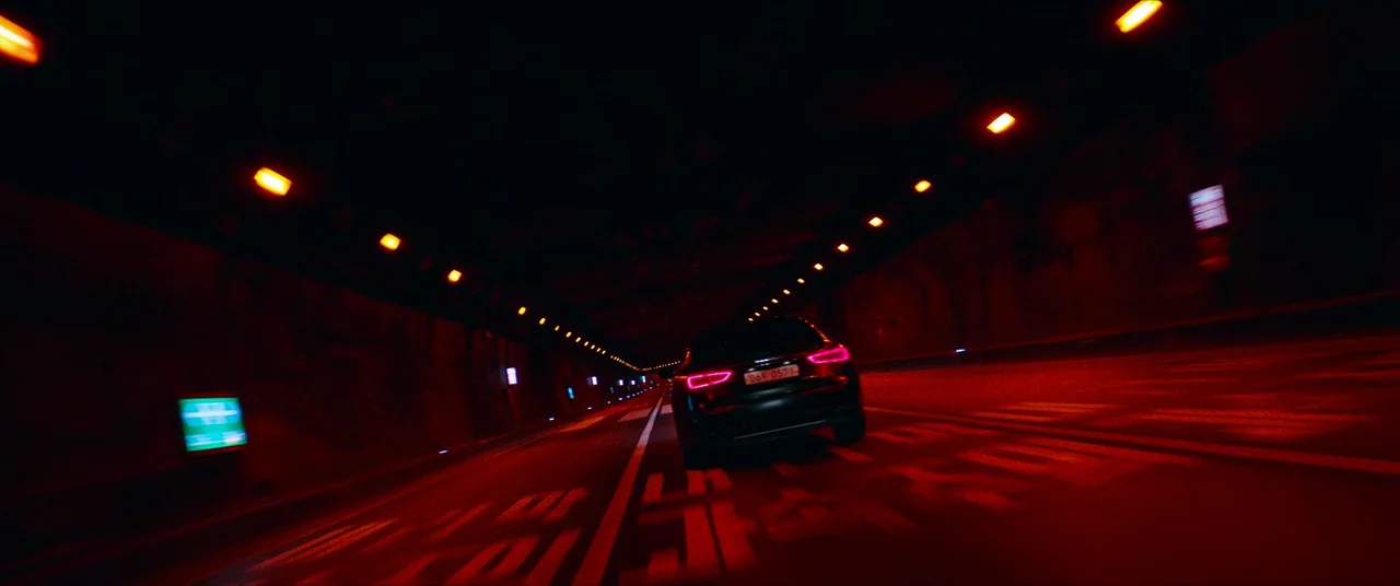 The Divine Fury (2019) movie still: A high-speed pursuit or late-night escape through a desolate, illuminated tunnel. The rhythmic flash of orange…
